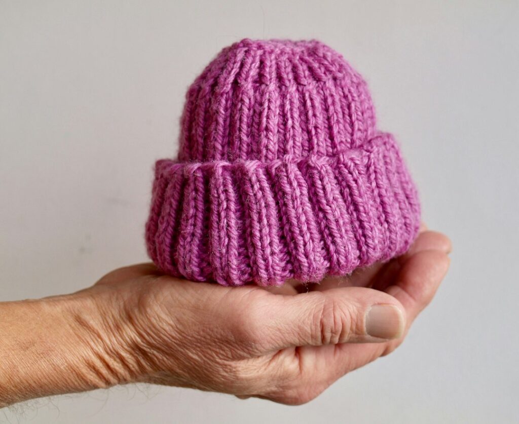 Hand holding a soft pink handmade baby hat