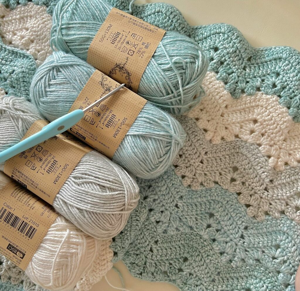 Three balls of yarn and a crochet hook on a soft blanket