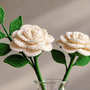 Two ivory handmade crochet roses with green crocheted leaves