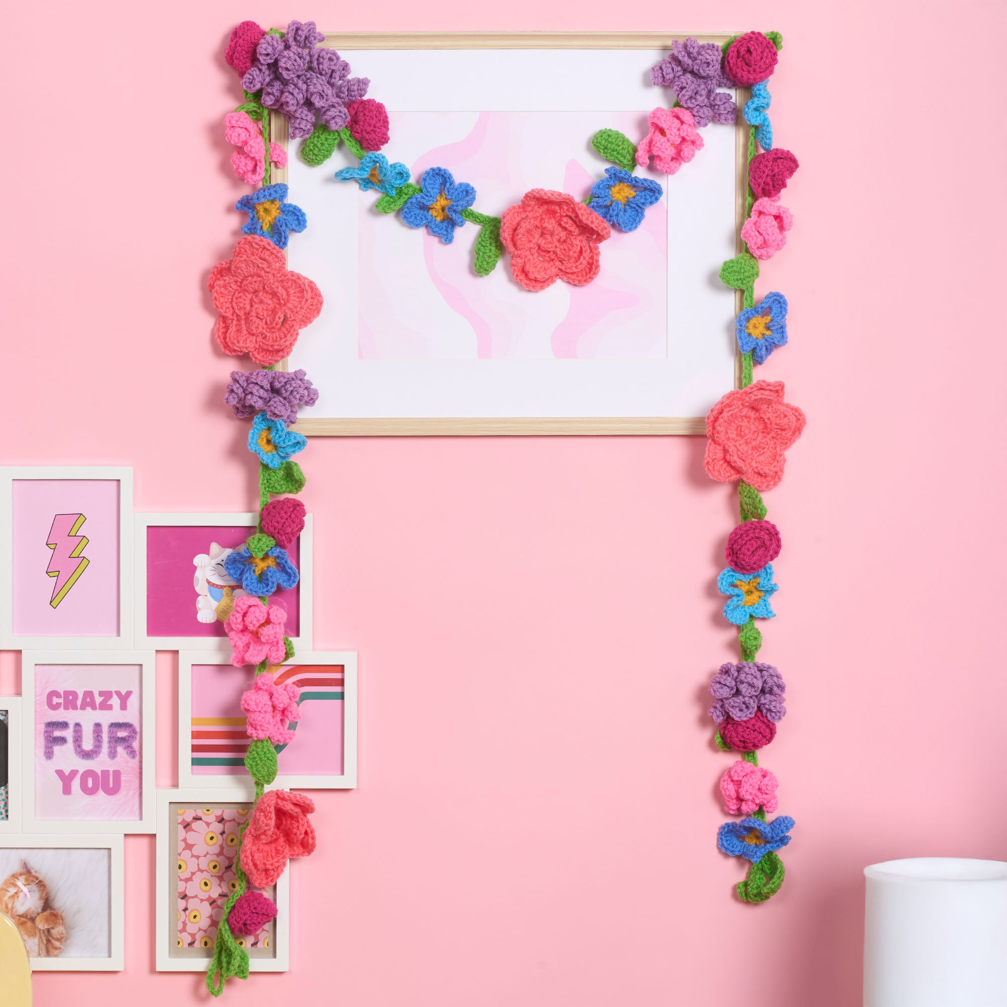 Colorful crochet flower garland hanging around a mirror on a pink wall