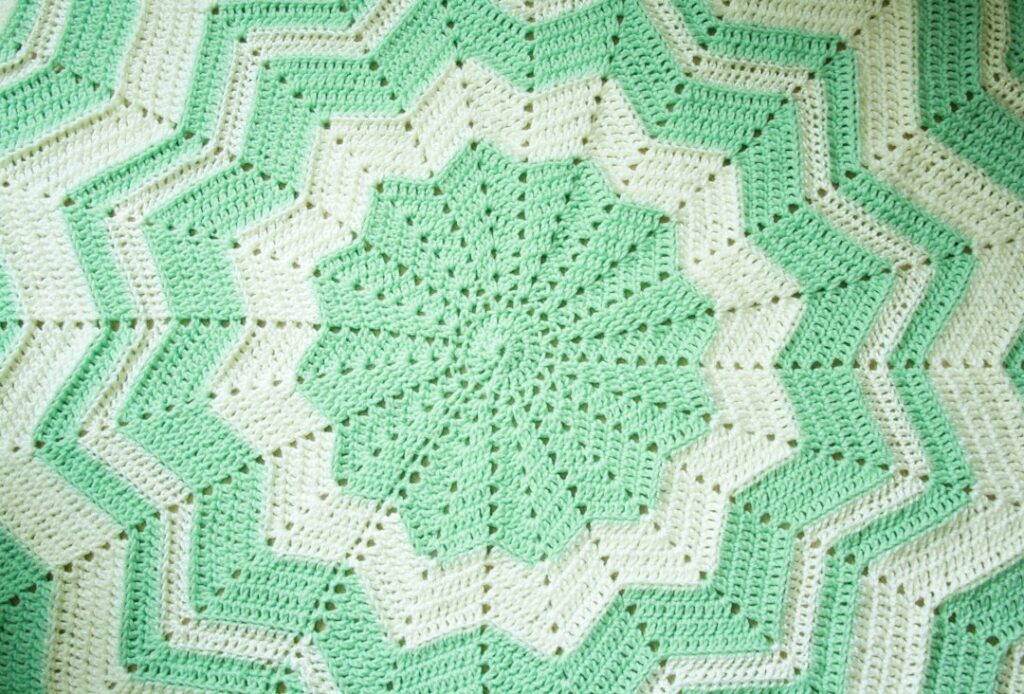 Green and white crocheted blanket arranged on a bed