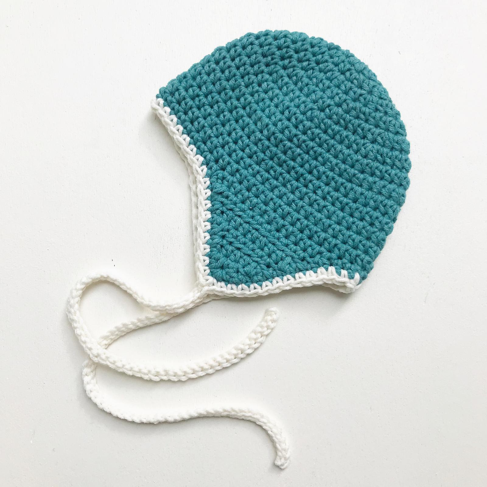Teal crochet baby bonnet with cream edging and ties by Inez de Goede