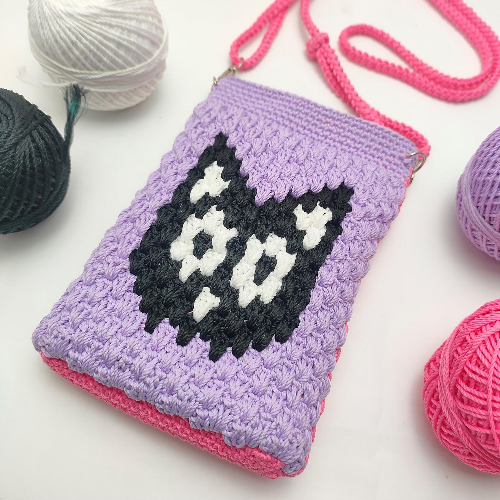 Purple crochet phone bag with a black and white cat-face motif and pink strap