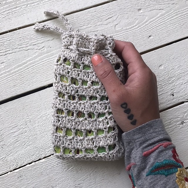 Gray eyelet crochet drawstring pouch held in a hand by Annie Lupton