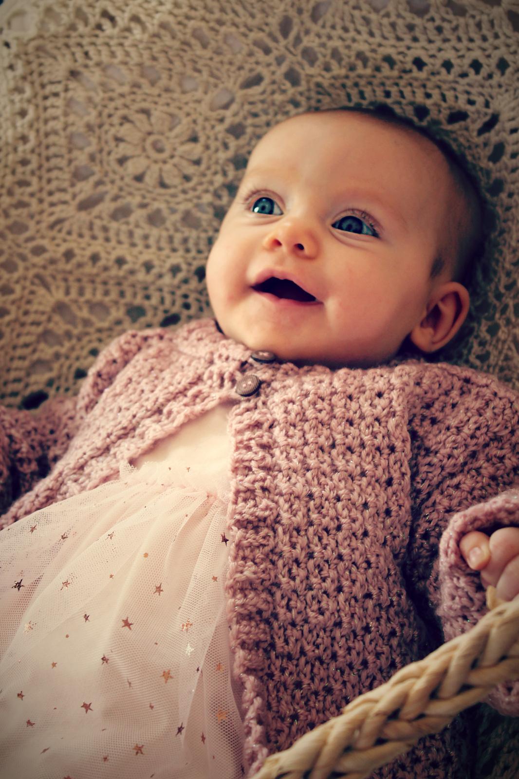 Baby wearing a pale pink crochet cardigan with a faux-cable texture
