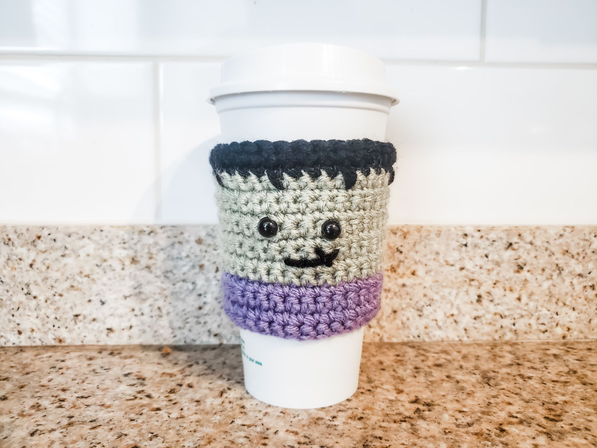 Green Frankenstein crochet coffee cozy with dark hair and purple trim by Heather Corinne