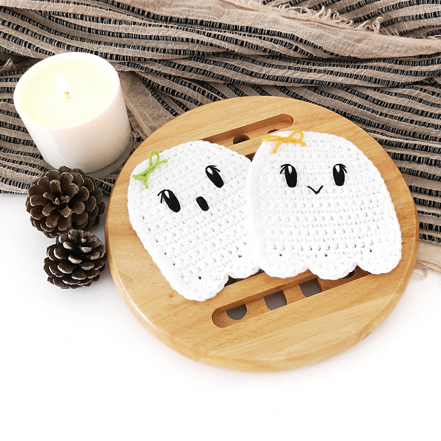Two white crochet ghost coasters with embroidered faces by Stitch by Fay