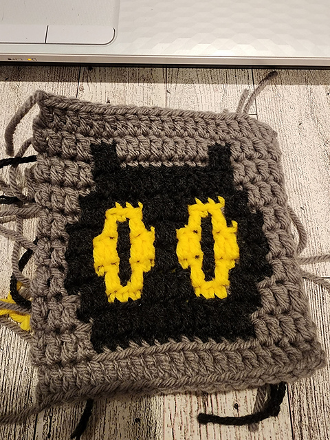 Crochet Halloween coaster with a black cat shape and yellow eyes by Mirian Valencia