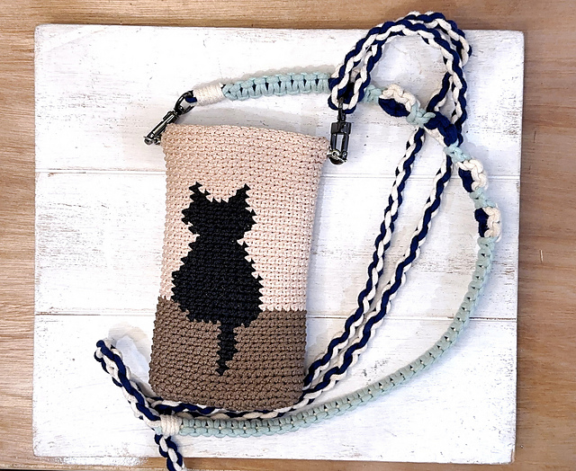 Light crochet phone pouch with a dark cat silhouette and a contrasting strap