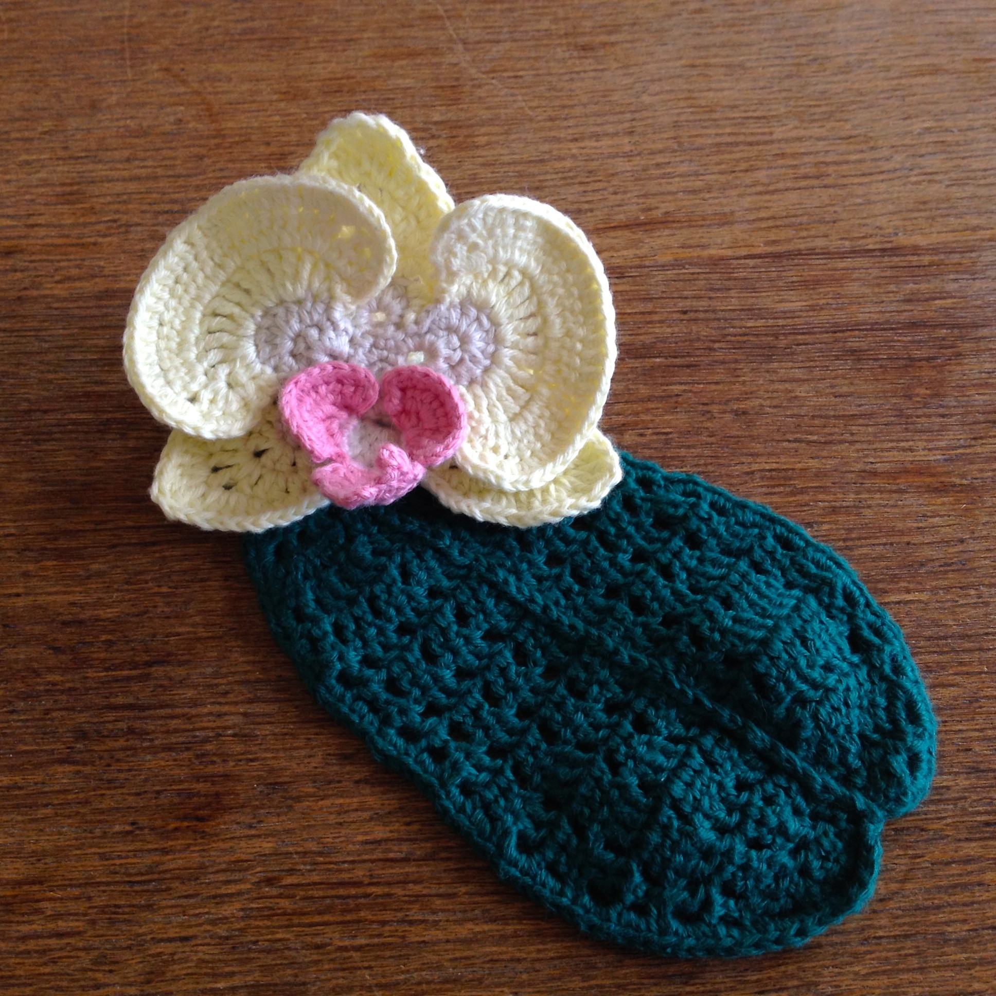 White crocheted orchid flower with a pink center shown on a blue accessory