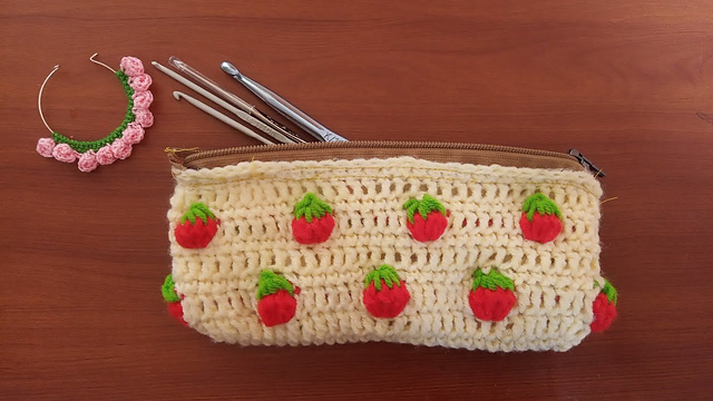 Crochet pencil pouch with small red strawberry motifs on a light background