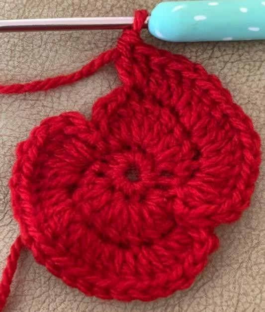 Red crochet poppy being shaped from its circular center