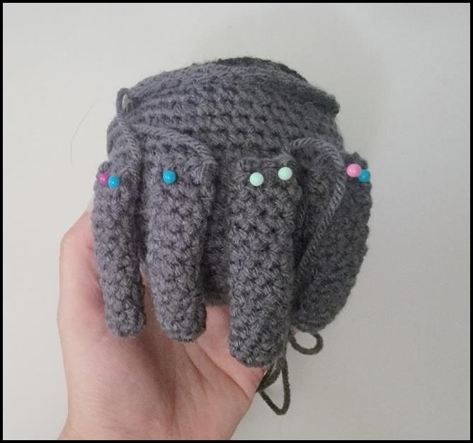 Pinning four crochet spider legs onto one side of the pot