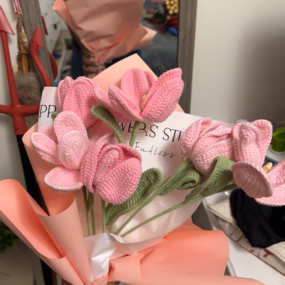 Bouquet of pink open and closed crochet flowers with pointed green leaves