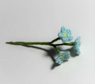 Three tiny blue crochet forget-me-not flowers on a green wrapped stem