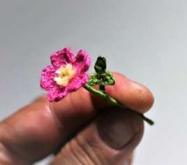Miniature pink crochet wild rose with yellow stamens and a green leaf