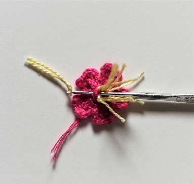 Yellow thread stamens being attached to a pink crochet wild rose
